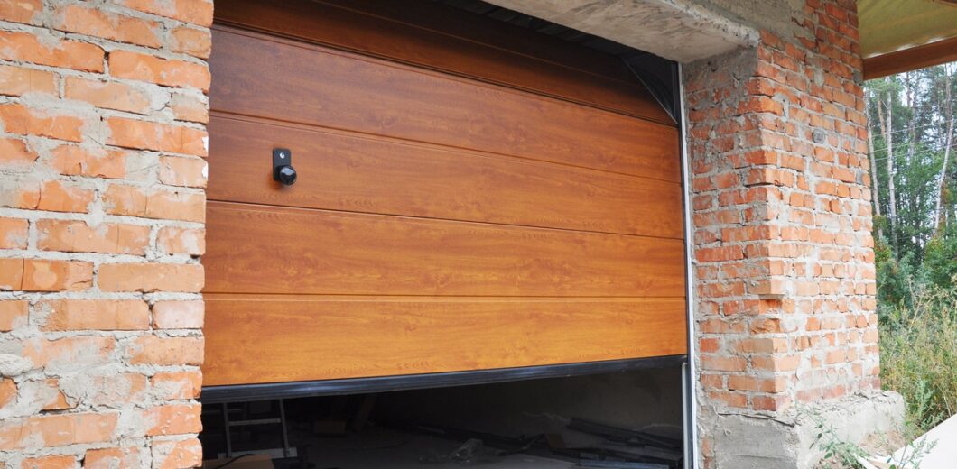 Partially open wooden garage door on a brick garage under construction, with building materials scattered on the unfinished concrete floor.