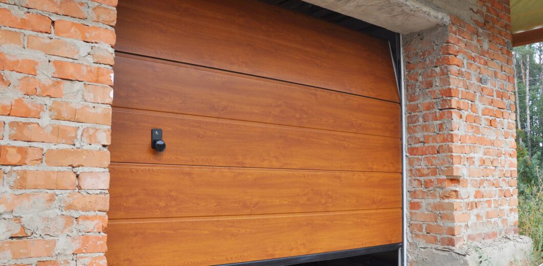 A partially opened wooden garage door is installed in a brick wall under construction, with some unfinished areas visible around the door frame.