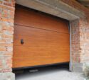 A partially opened wooden garage door is installed in a brick wall under construction, with some unfinished areas visible around the door frame.