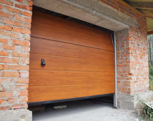 A partially opened wooden garage door is installed in a brick wall under construction, with some unfinished areas visible around the door frame.