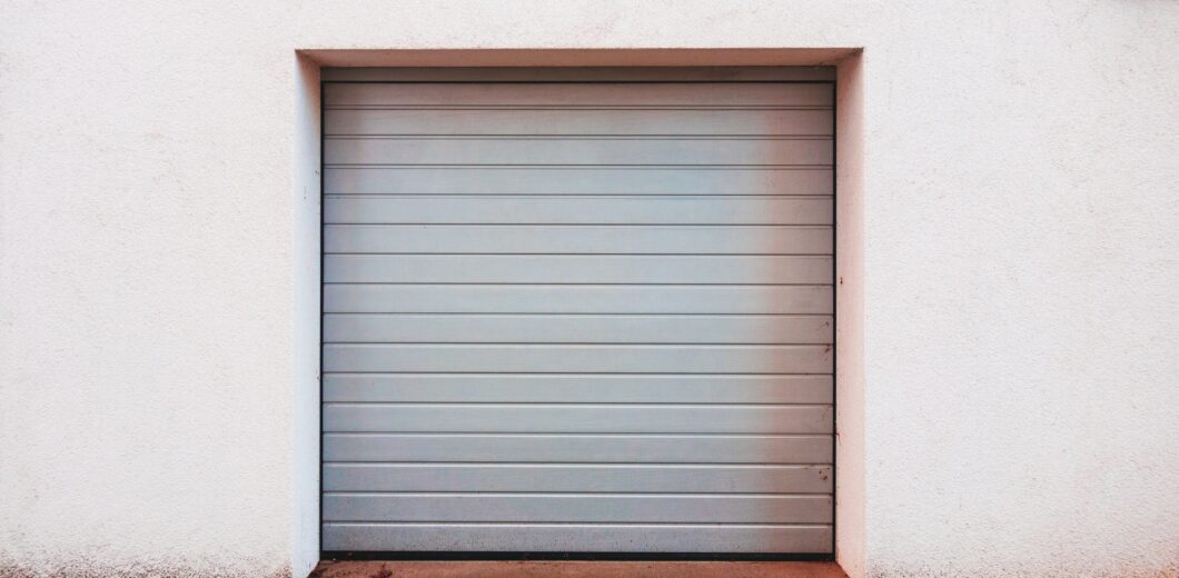 A closed gray garage door set in a white wall, with a cobblestone driveway in front.