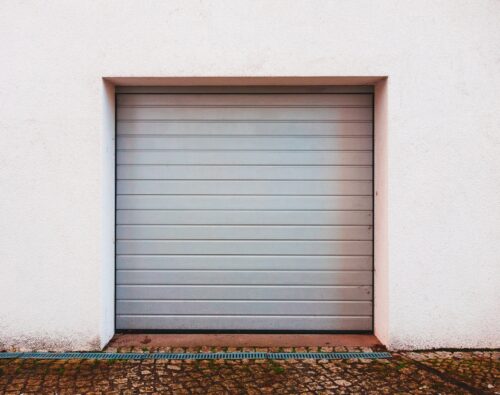 A closed gray garage door set in a white wall, with a cobblestone driveway in front.