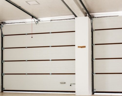 A clean, empty garage with closed white sectional doors, horizontal brown trim, and a red pull cord hanging from the ceiling.