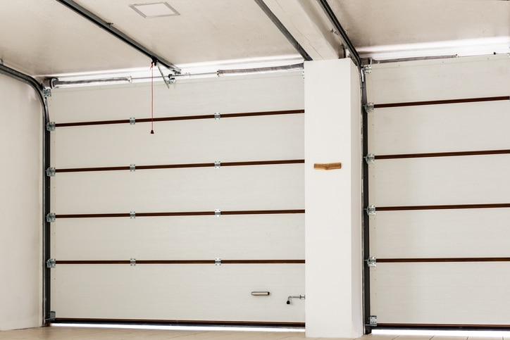 A clean, empty garage with closed white sectional doors, horizontal brown trim, and a red pull cord hanging from the ceiling.
