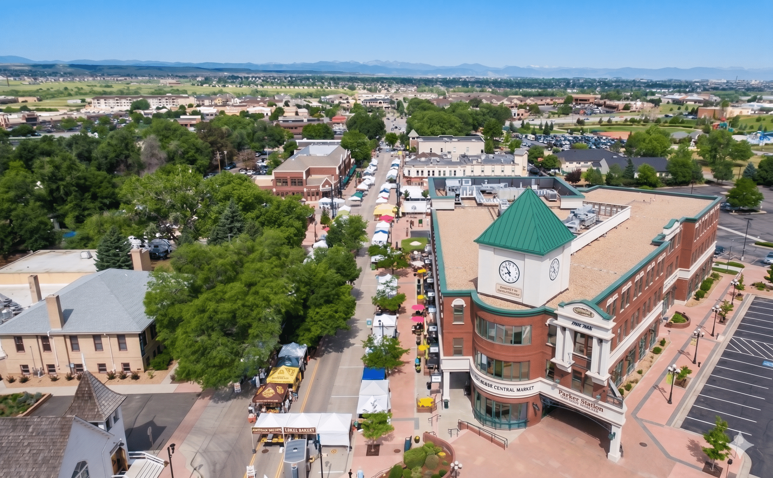 Aerial view of downtown Parker, Colorado showing the clock tower building, tree-lined streets, and an outdoor market event.