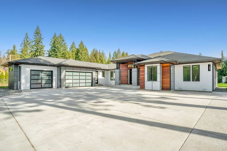 White and brown wooden house with an attached garage near green trees