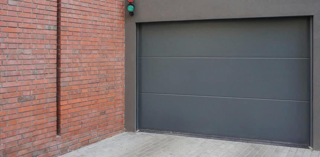 Grey residential garage door next to a brick wall