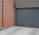 Grey residential garage door next to a brick wall
