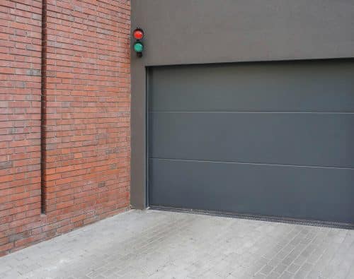 Grey residential garage door next to a brick wall