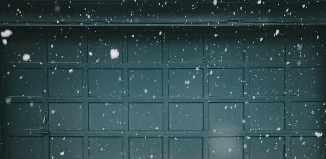 Snow falling in front of a teal paneled garage door