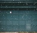 Snow falling in front of a teal paneled garage door