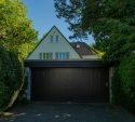 Wide dark garage door on a home framed by tall hedges