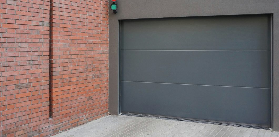 Modern grey sectional garage door beside a brick wall