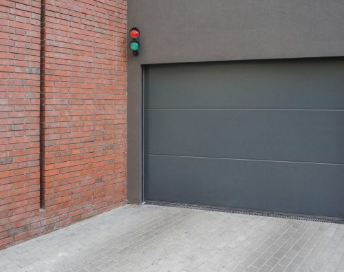 Modern grey sectional garage door beside a brick wall