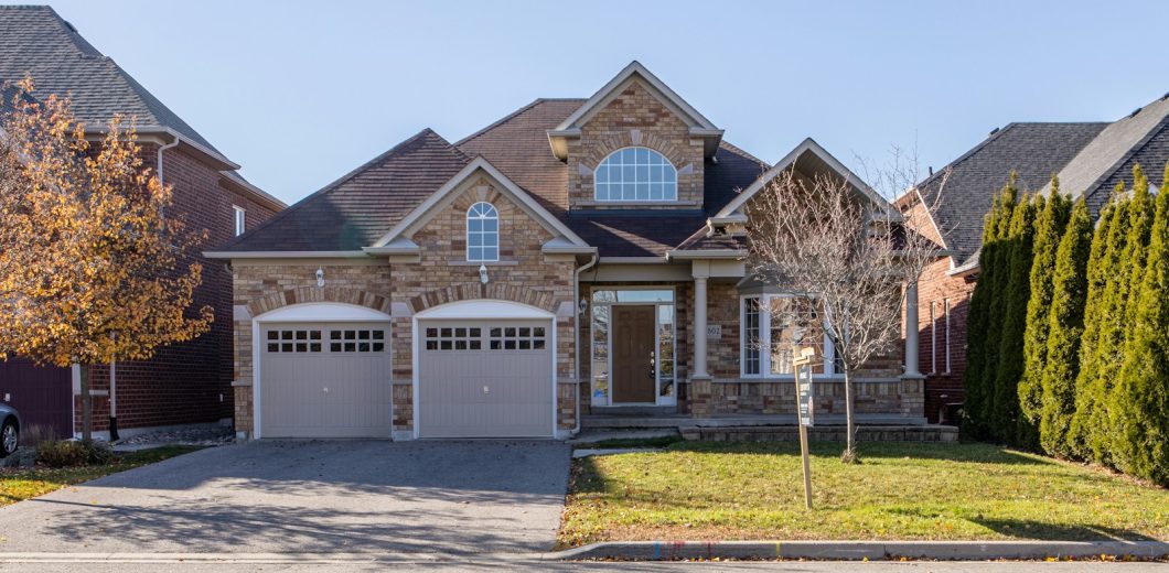 Stone home with two garage doors framed by a golden autumn tree