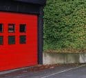 Bright red painted garage door beside an ivy covered wall